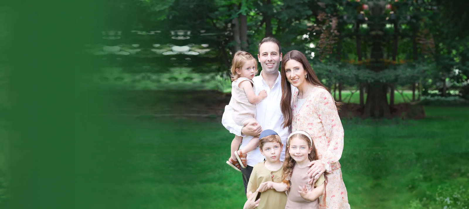 A family of four, including two adults and two children, poses for a photo in an outdoor park setting.