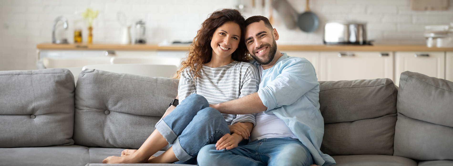 A man and a woman sitting on a couch, smiling at the camera.