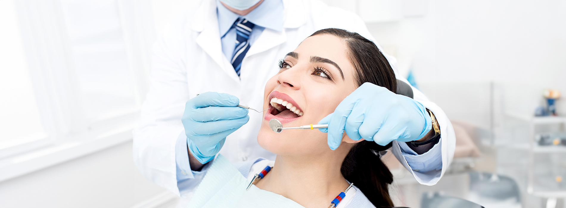 A dental professional is performing a procedure on a patient s teeth, with the patient smiling and lying in a chair.