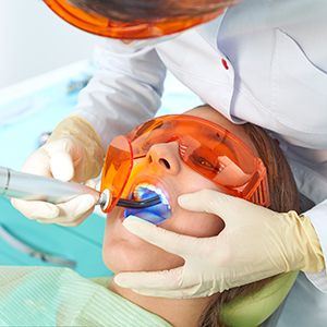 A dental professional performing a dental procedure on a patient wearing protective eyewear.