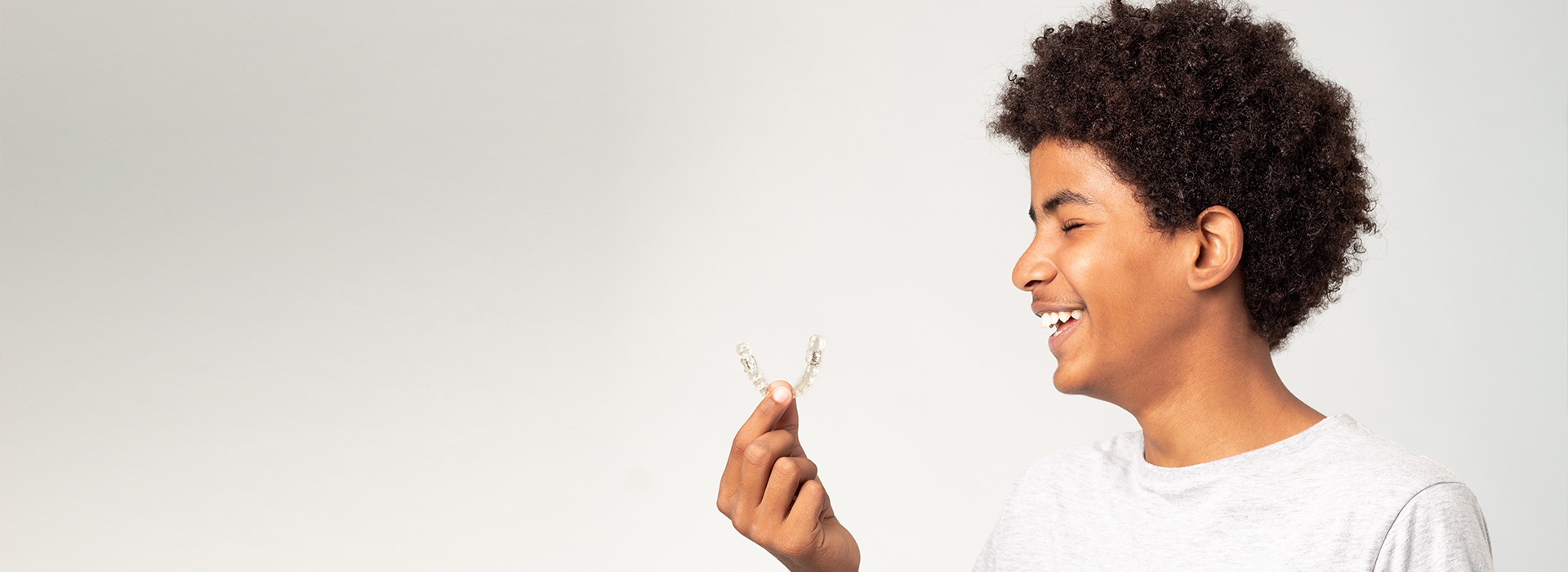 The image features a person, likely a young adult, smiling and holding a small object, possibly a feather or flower, against a plain background.