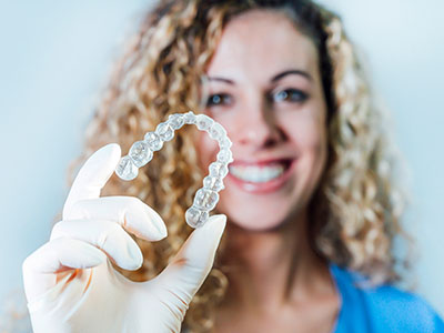 A woman wearing a white glove is holding up a transparent dental retainer with her left hand.