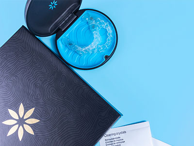 A black and gold toothbrush with a blue toothpaste tube next to an open box of dental floss on a light blue background.