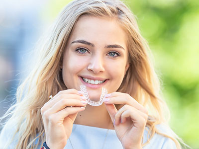 A woman is holding a toothbrush up to her mouth, smiling at the camera.