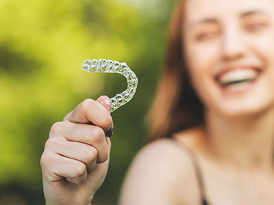 A smiling person holding a transparent toothbrush with bristles.