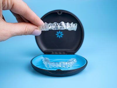 The image shows a person s hand holding an open mouthguard with clear, transparent bristles inside, which is placed on top of a blue and black box that appears to be a dental appliance or tool.