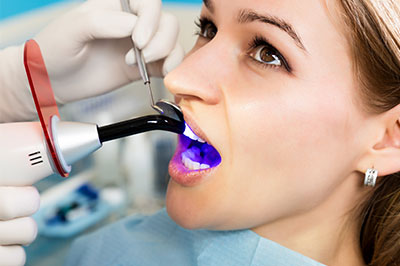 A woman receiving a dental treatment, with a dentist using an ultrasonic scaler on her teeth.