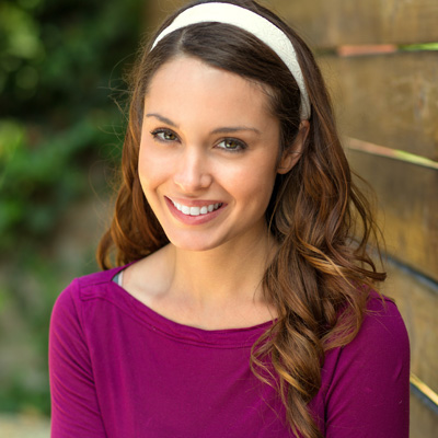 A woman with long hair wearing a purple top and headband, smiling at the camera.