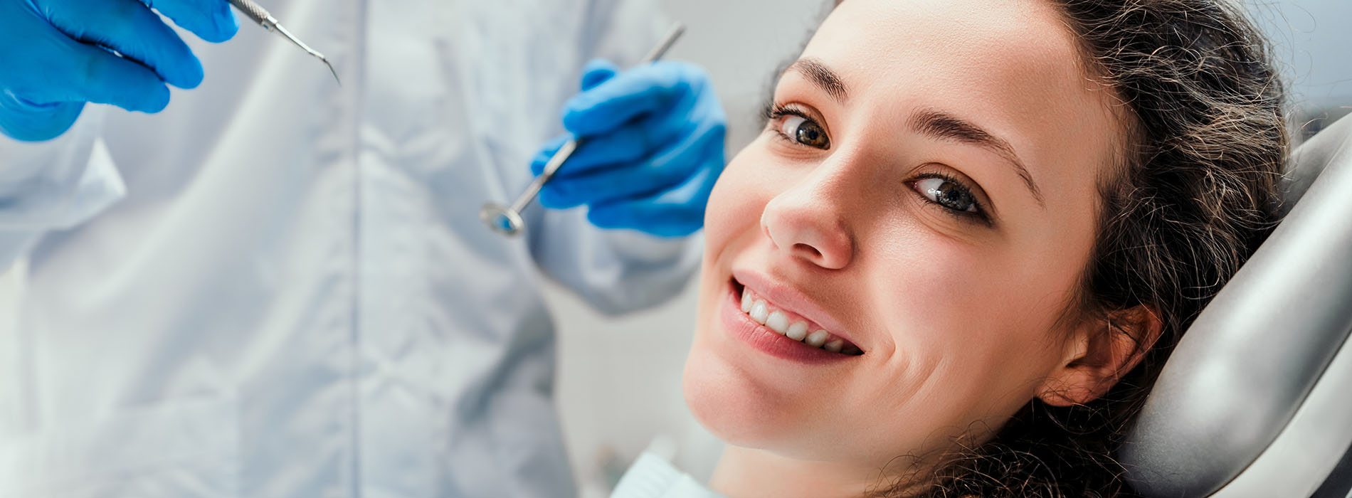 The image shows a woman seated in a dental chair, receiving dental care from a dentist, with a focus on the dental instruments and equipment being used.