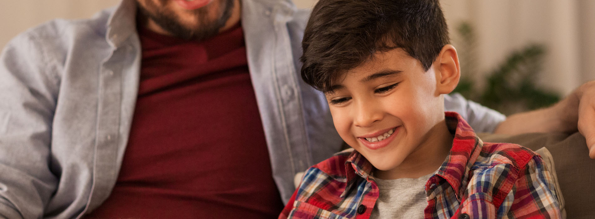 A man and a young boy are sitting on a couch, smiling at the camera.