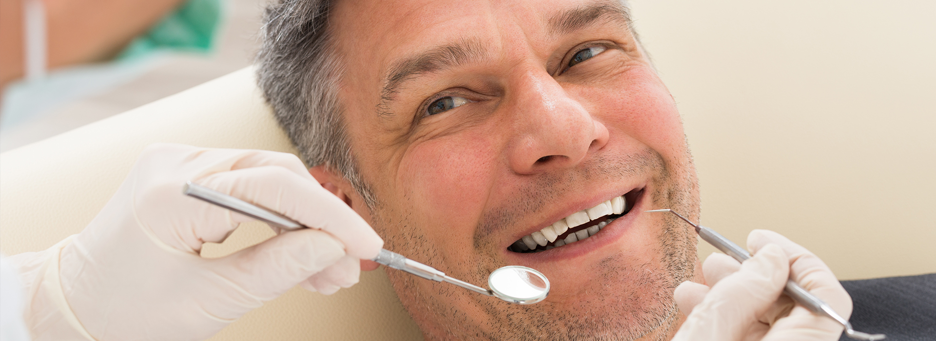 The image shows a man in a dental chair receiving dental treatment, with a dentist working on his teeth.