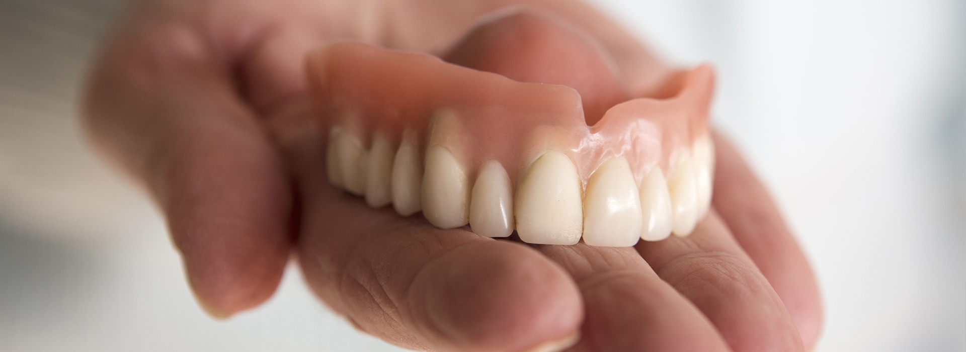 The image shows a person holding an artificial human mouth with teeth, likely for dental education or demonstration purposes.