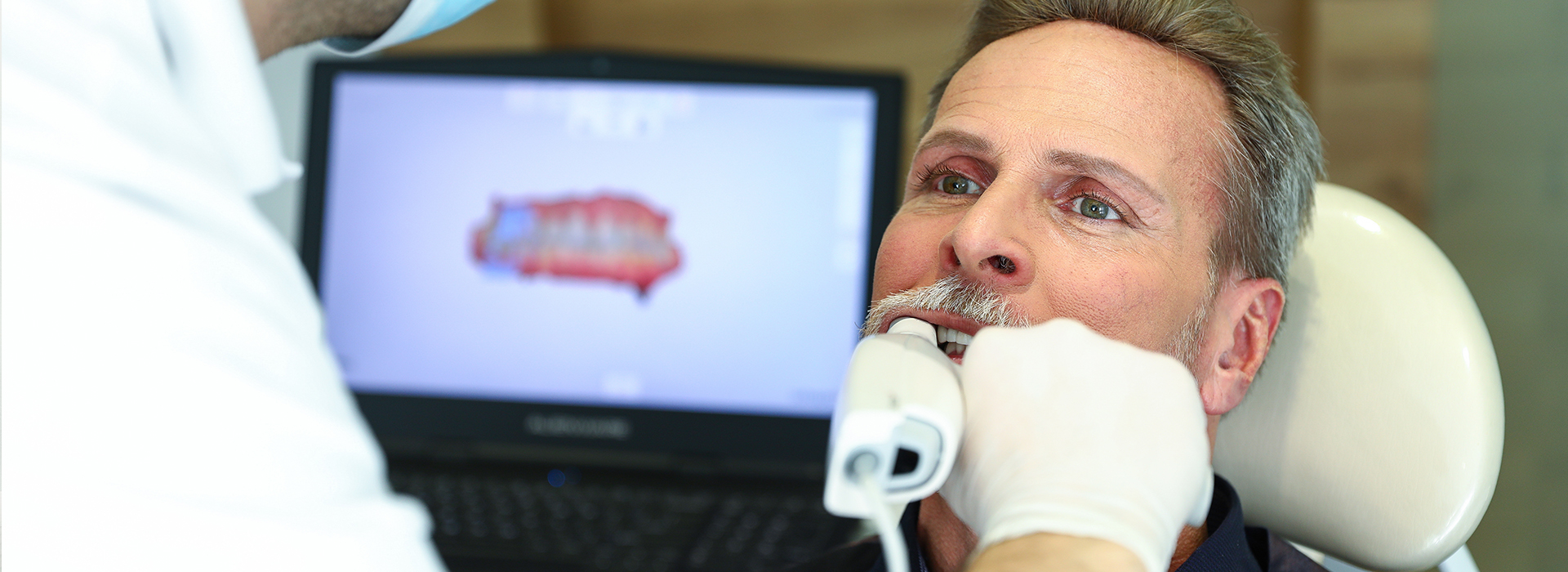 The image shows a medical professional performing a dental procedure on a patient, with the patient seated in a chair and wearing a surgical mask.