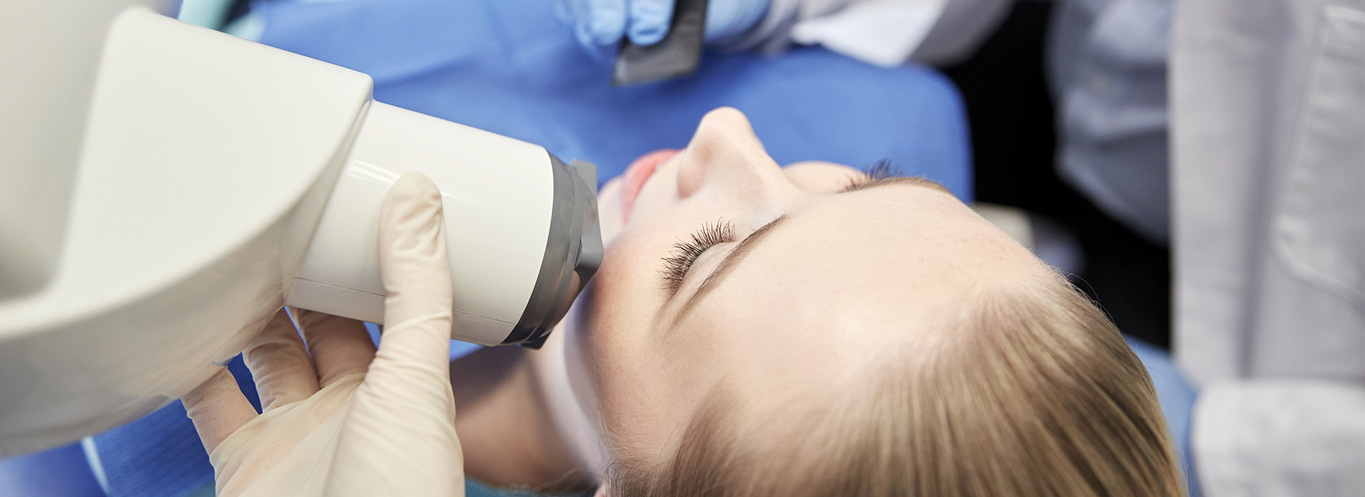 A person receiving a dental implant or similar medical procedure, with a device attached to their face and a medical professional operating the equipment.