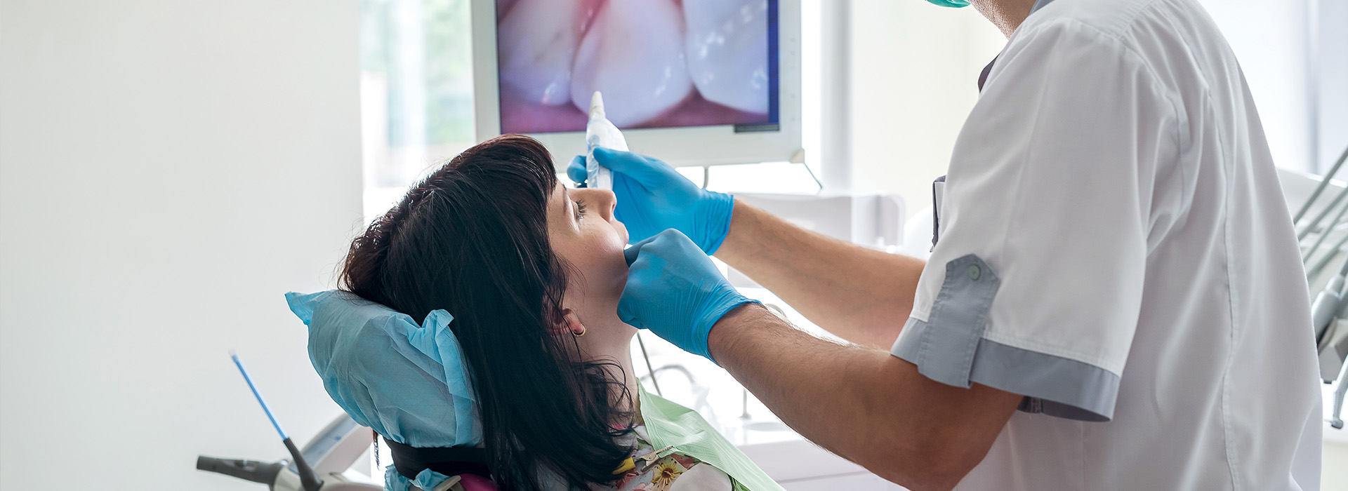 A dental professional performing a procedure on a patient, with the dentist wearing a face mask and blue gloves.