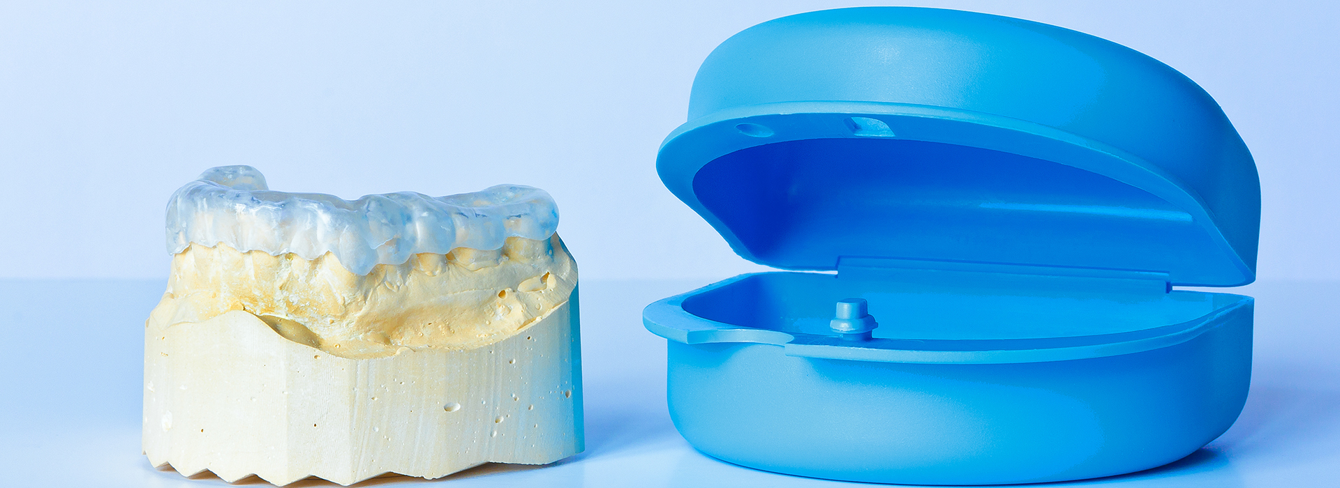 The image shows a transparent blue dental mold on the right and a yellow dental mold on the left, placed side by side against a white background.