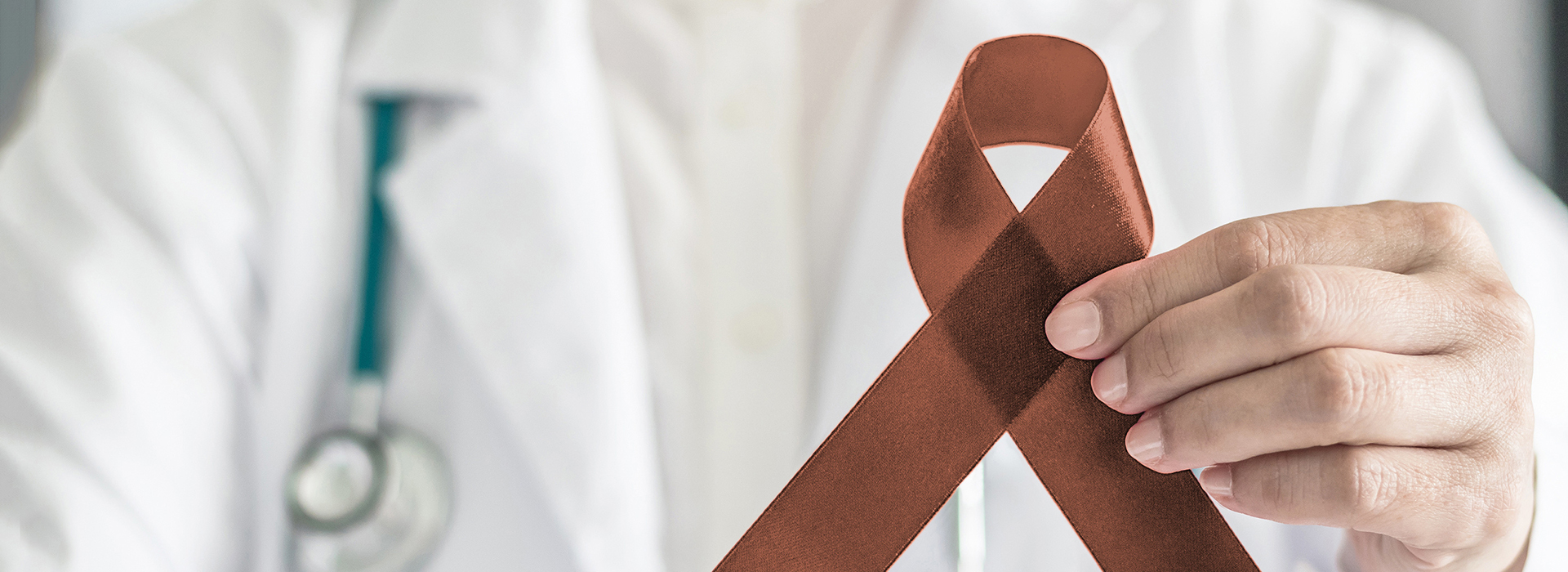 The image shows a person holding a brown ribbon with a red symbol, possibly indicating awareness for a cause or disease, while standing in front of a medical professional who is wearing a stethoscope.