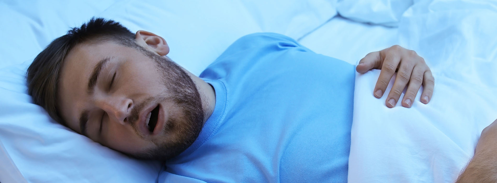 Man lying in bed, holding a pillow with his face on it.