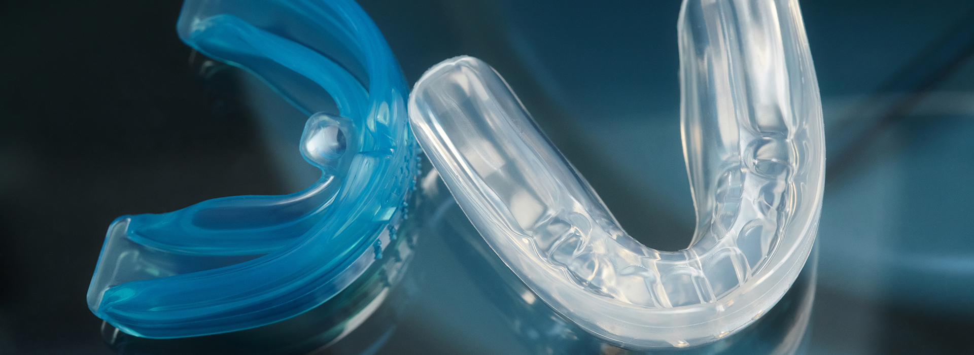 The image features a clear, plastic dental retainer with a blue tint in the foreground and a blurred background that appears to be a dark surface.