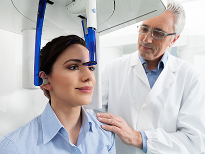 A woman receiving a facial treatment in a medical setting, with a male technician adjusting the device over her head.