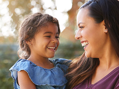 A woman and a young child are smiling at the camera, with the woman holding the child in her arms.