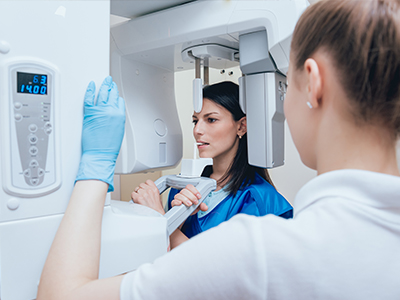 A woman in a blue uniform is standing next to a large white 3D scanner, with another person looking at the scanner.