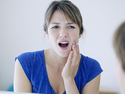 Woman in blue shirt making a disapproving facial expression, possibly reacting to her own reflection.