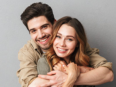 A man and a woman are hugging each other closely, both smiling at the camera.