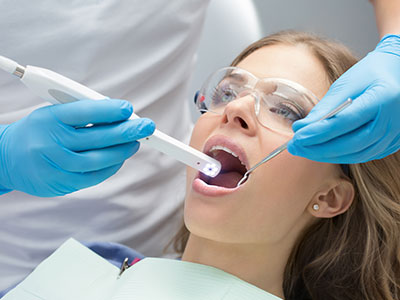 A woman receiving dental treatment, with a dentist using an electric toothbrush and the patient s mouth open wide.