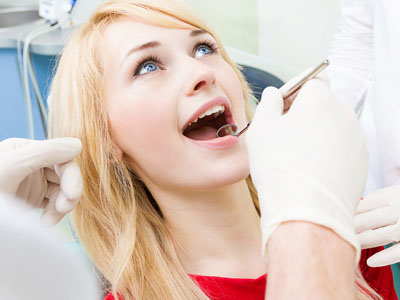 A woman seated in a dental chair, smiling broadly, with her mouth open as if she s undergoing a dental procedure or being photographed for it.