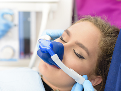 An adult female undergoing a medical procedure, with oxygen mask in place and receiving attention from a healthcare professional.