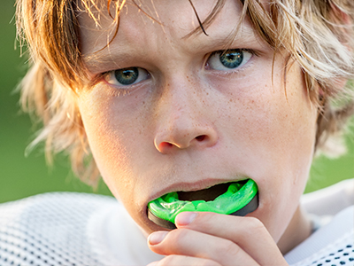 A young male athlete with blonde hair and a determined expression, holding a mouthguard in his hand.