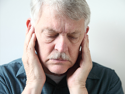 The image shows an older man with a mustache, wearing glasses and holding his hand to his ear, seemingly in pain or discomfort.